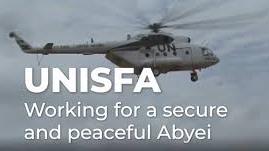 A helicopter flying against a dark grey sky with the words "Working for a secure and peaceful Abyei"