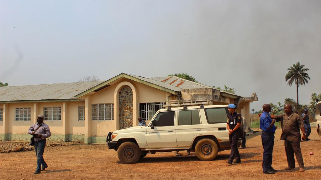 A few staff members standing by a car and a house on the field