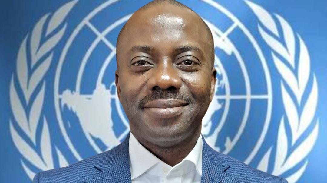 A headshot of a man in a suit stands in front of the UN logo