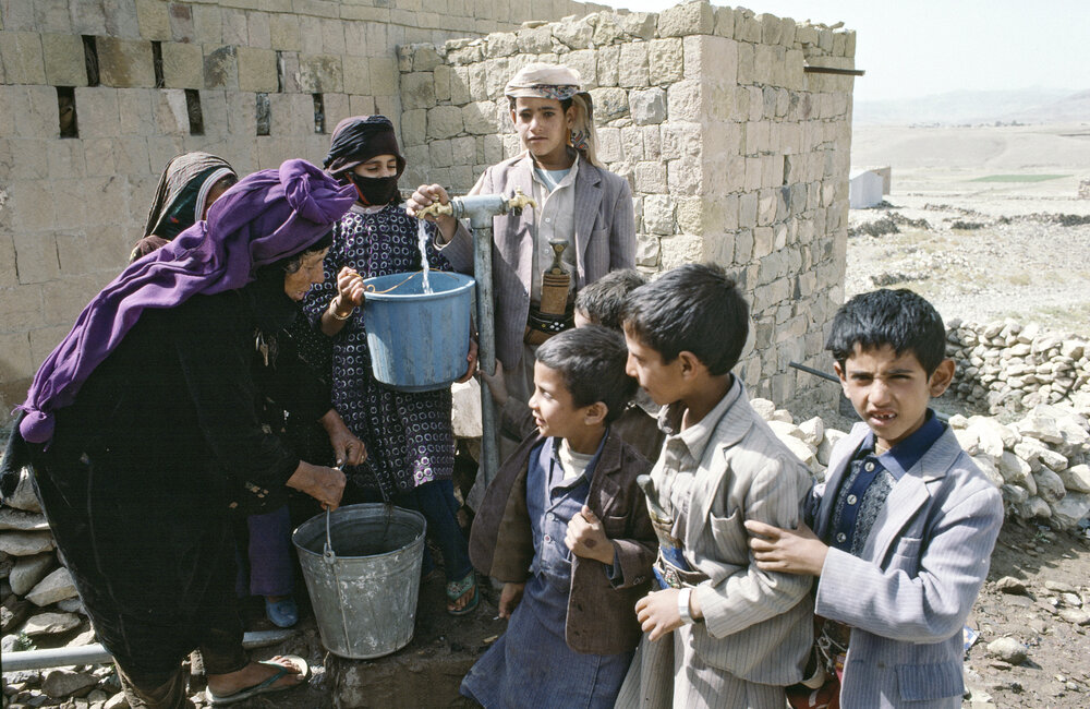 Children helping an old woman fill her containers with water from a community pump in Dobra Khira near Sana'a. 1985. UN Photo/UN Photo Library.